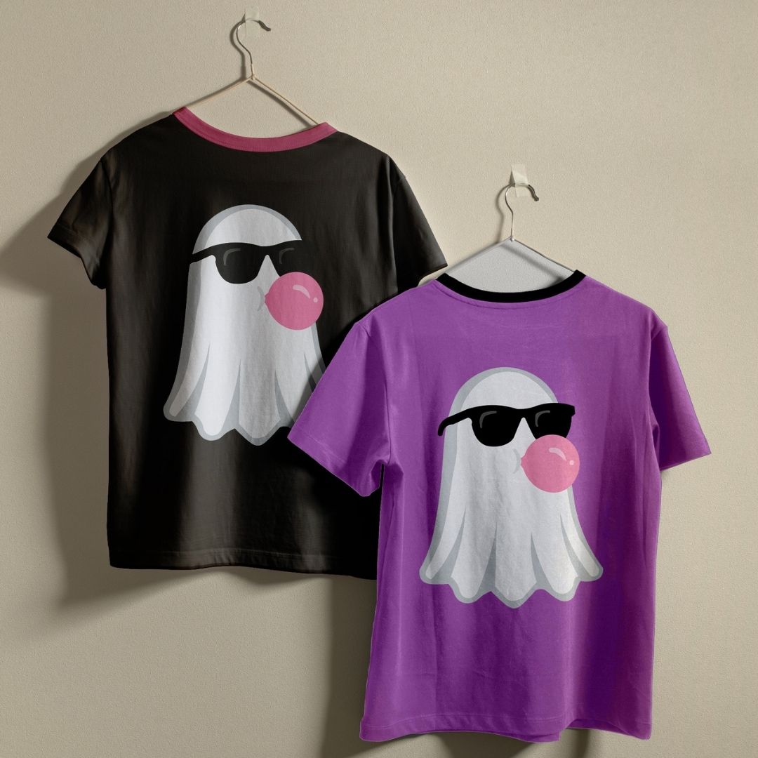 Two ringer t-shirts hanging on hangers against a beige wall. The left shirt is black with a pink collar and features a white ghost graphic wearing black sunglasses and blowing a pink bubblegum bubble.