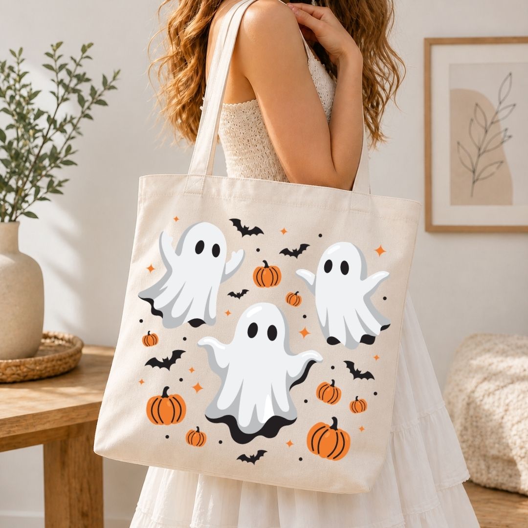 Woman holding a canvas tote bag printed with a cute Halloween ghosts and pumpkins graphic design.