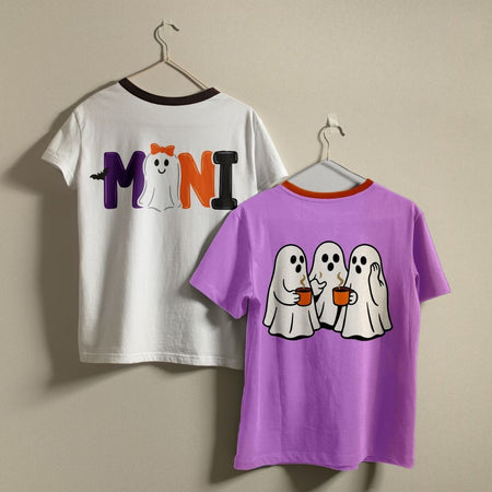 Two children's short-sleeve T-shirts hanging on hangers against a plain beige wall. The left shirt is white with a dark brown collar trim and the word 'MINI' printed across the back in purple, white, and orange, with a small ghost.