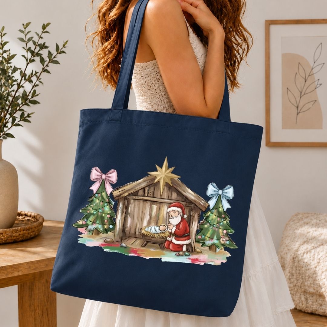 A navy blue canvas tote bag with a Christmas nativity scene print, carried on the shoulder of a woman in a white dress in a cozy indoor setting.