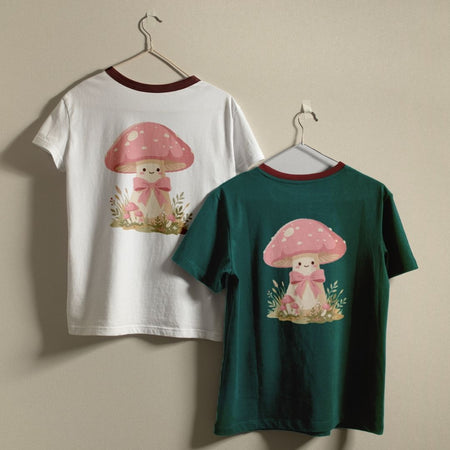 Two t-shirts, one white and one green, with a pink mushroom design on a beige background.