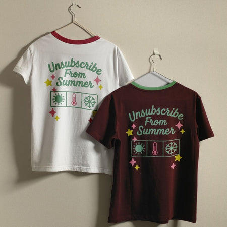 Two t-shirts with 'Unsubscribe From Summer' design on hangers against a beige wall.