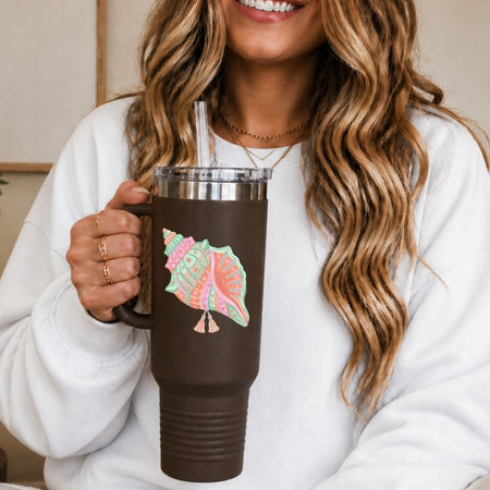 Person holding a brown mug with a colorful shell design, wearing a white sweater.