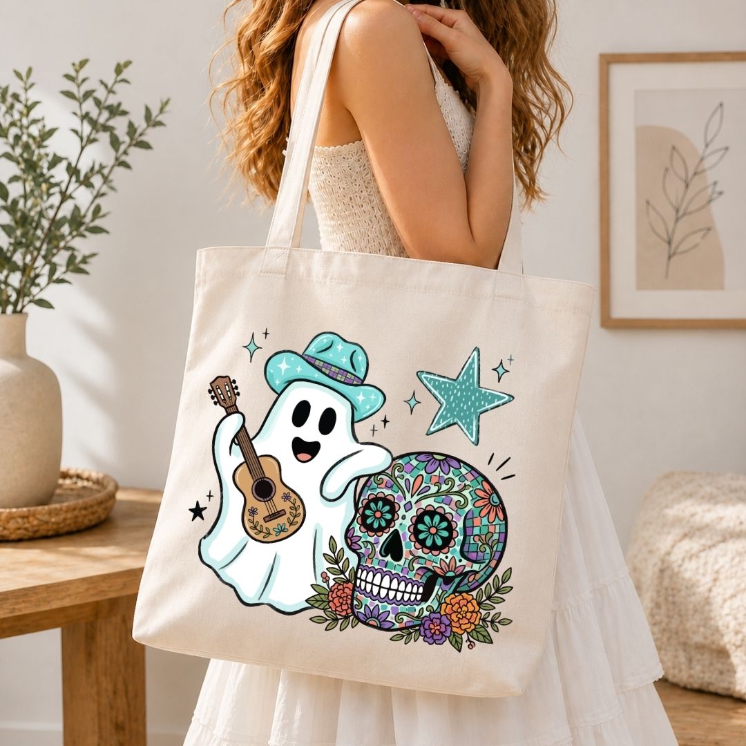 A person wearing a white dress and carrying a natural canvas tote bag printed with the ghost playing guitar and sugar skull Halloween graphic.