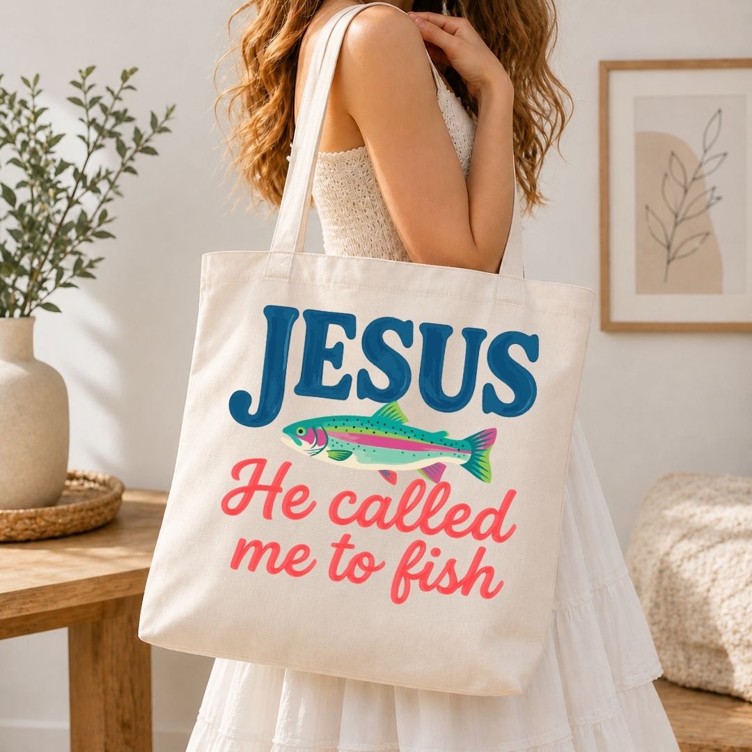 A woman carrying a cream-colored canvas tote bag over her shoulder printed with a large, vibrant "Jesus He Called Me to Fish" logo.