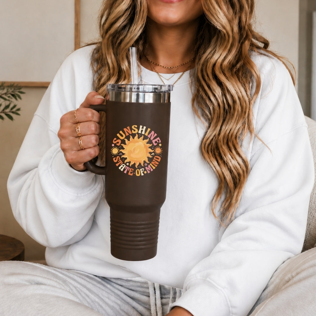 Person holding a brown mug with a sun design and text, wearing a white sweatshirt.
