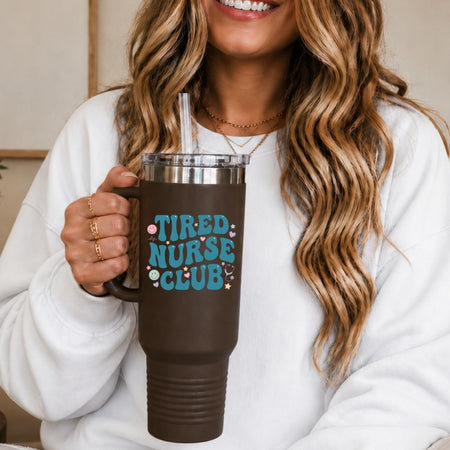 Person holding a brown mug with 'Tired Nurse Club' text, smiling.