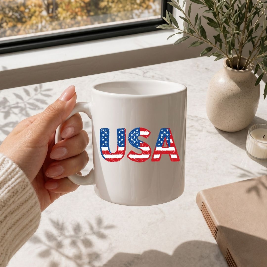 Hand holding a white mug with a soccer ball design, placed on a light surface with a plant and notebook in the background.