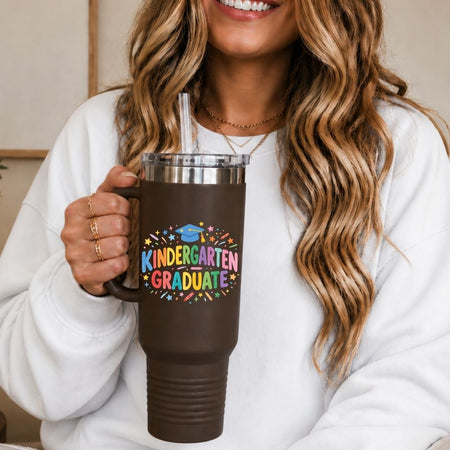 Person holding a brown mug with 'Kindergarten Graduate' text and colorful design.