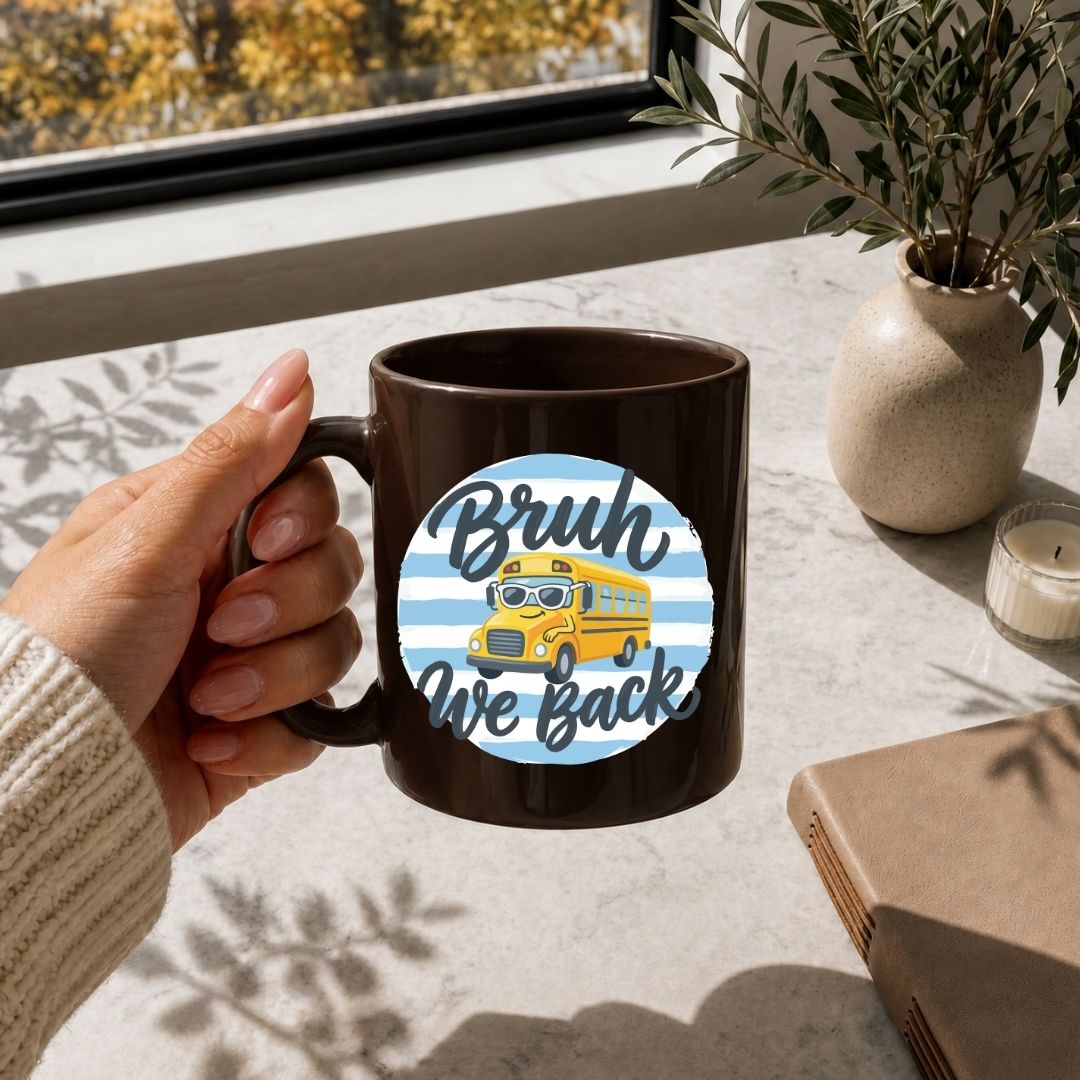 Person holding a mug with a 'Bruh We Back' design on a table with a window and plant in the background