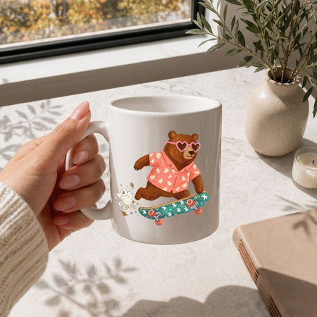 Hand holding a mug with a bear design on a table with a window and plant in the background