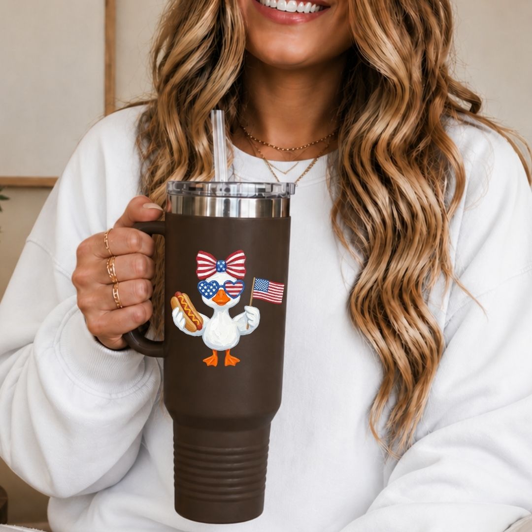 Person holding a brown insulated tumbler with a design of a duck wearing an American flag bow tie and holding an American flag hot dog.
