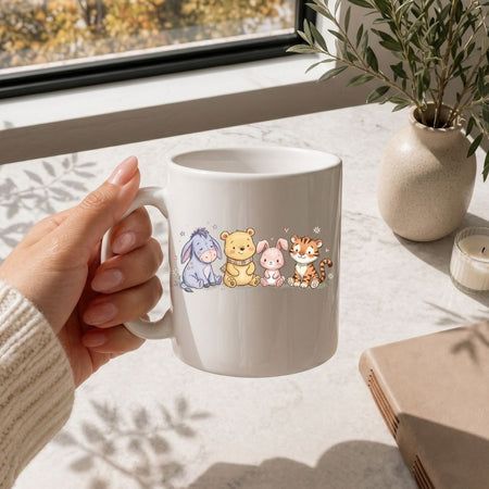 Hand holding a white mug with cartoon characters on a light surface with a window and plant in the background