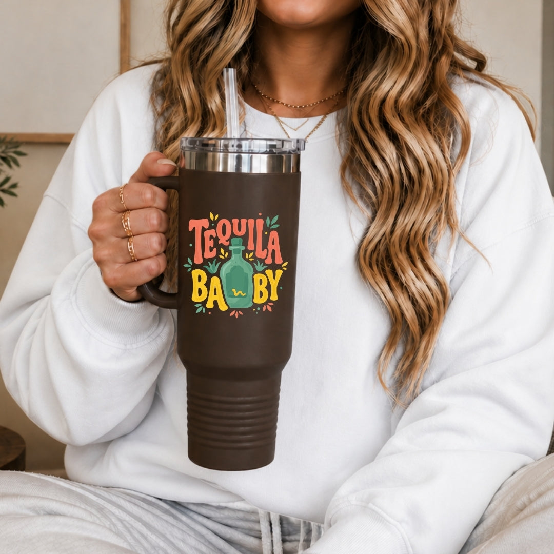 Person holding a brown mug with 'Tequila Baby' text and design.
