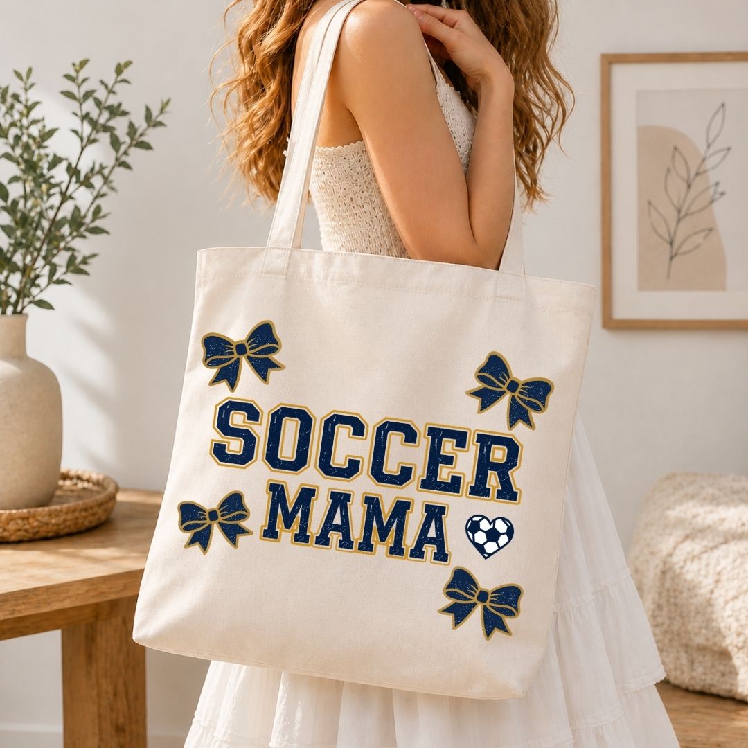 Person holding a tote bag with 'Soccer Mama' text and designs in a home setting