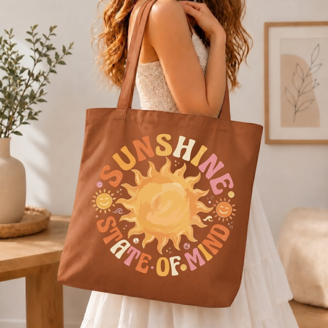 Person holding a brown tote bag with a sun design and 'Sunshine State of Mind' text.