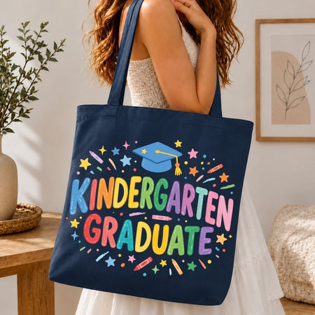 Navy tote bag with 'Kindergarten Graduate' text and colorful design held by a person indoors.
