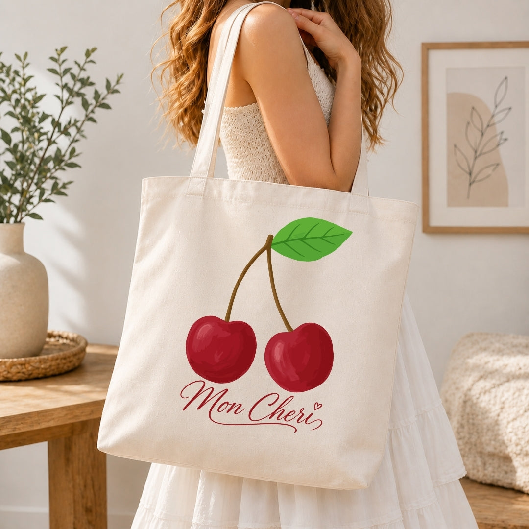 Person holding a tote bag with cherry design and 'Mon Cheri' text in a home setting.