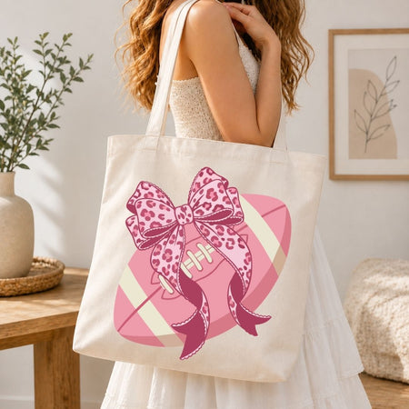 Person holding a tote bag with a pink bow design in a home setting