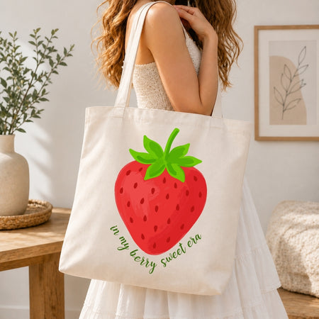 Person holding a tote bag with a strawberry design and text in a home setting