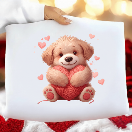 White pillow with a cartoon dog holding yarn and surrounded by hearts, held by a person against a blurred background.