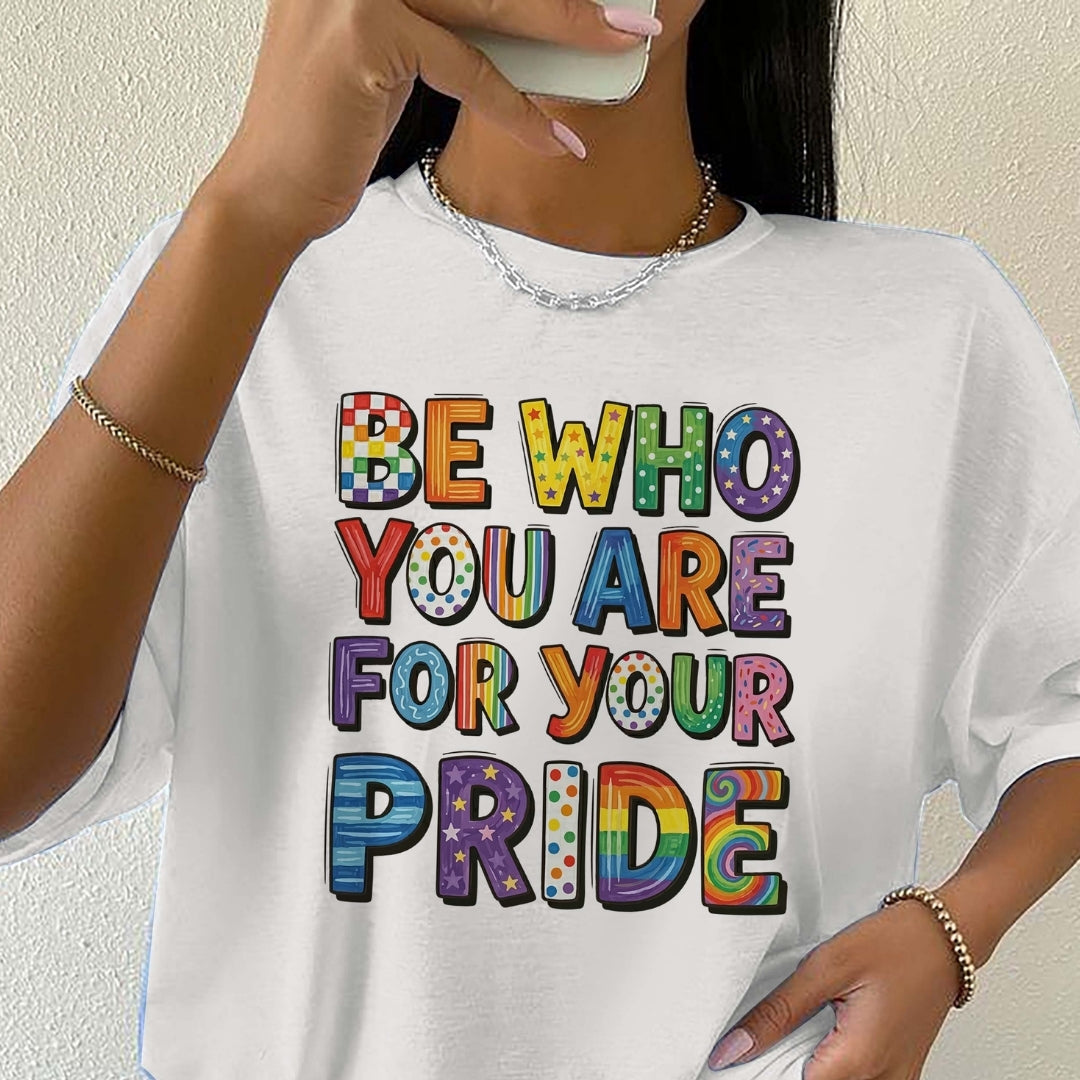 Person wearing a white t-shirt with colorful text 'BE WHO YOU ARE FOR YOUR PRIDE' against a plain background.