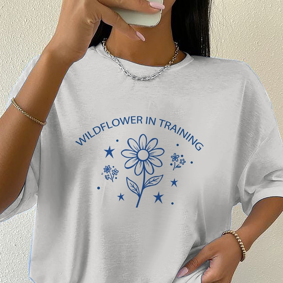 Person wearing a white t-shirt with 'Wildflower in Training' design.