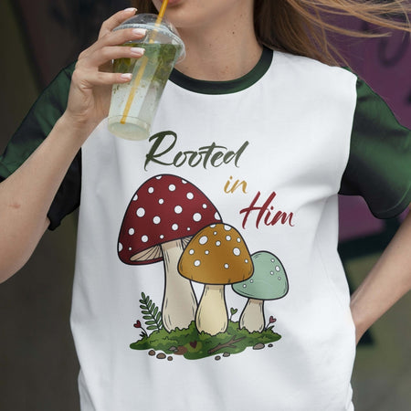 Person wearing a white t-shirt with mushroom design and 'Rooted in Him' text, holding a drink.