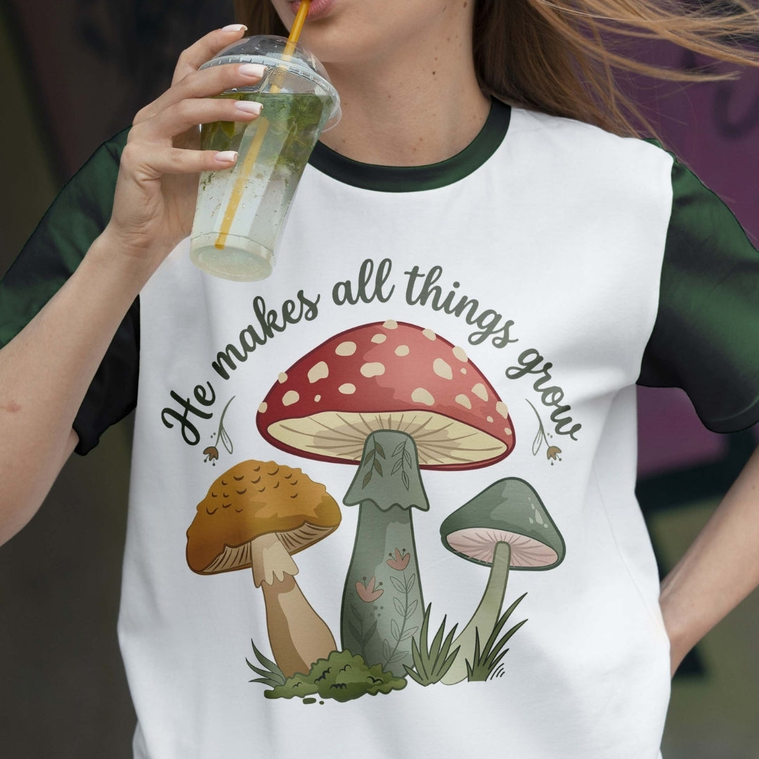 Person wearing a t-shirt with mushroom design and text, holding a drink.