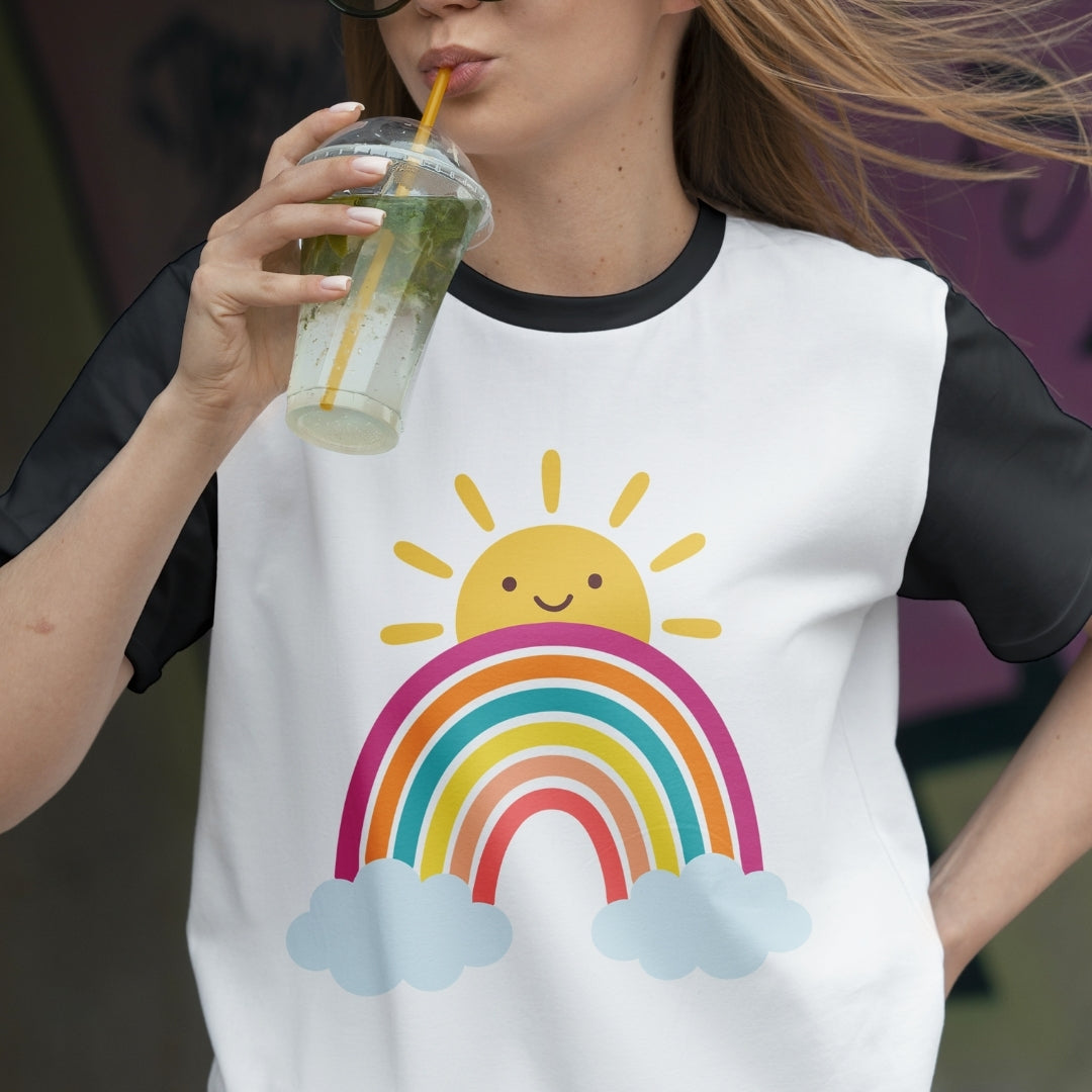 Person wearing a white t-shirt with a rainbow and sun design, holding a drink.