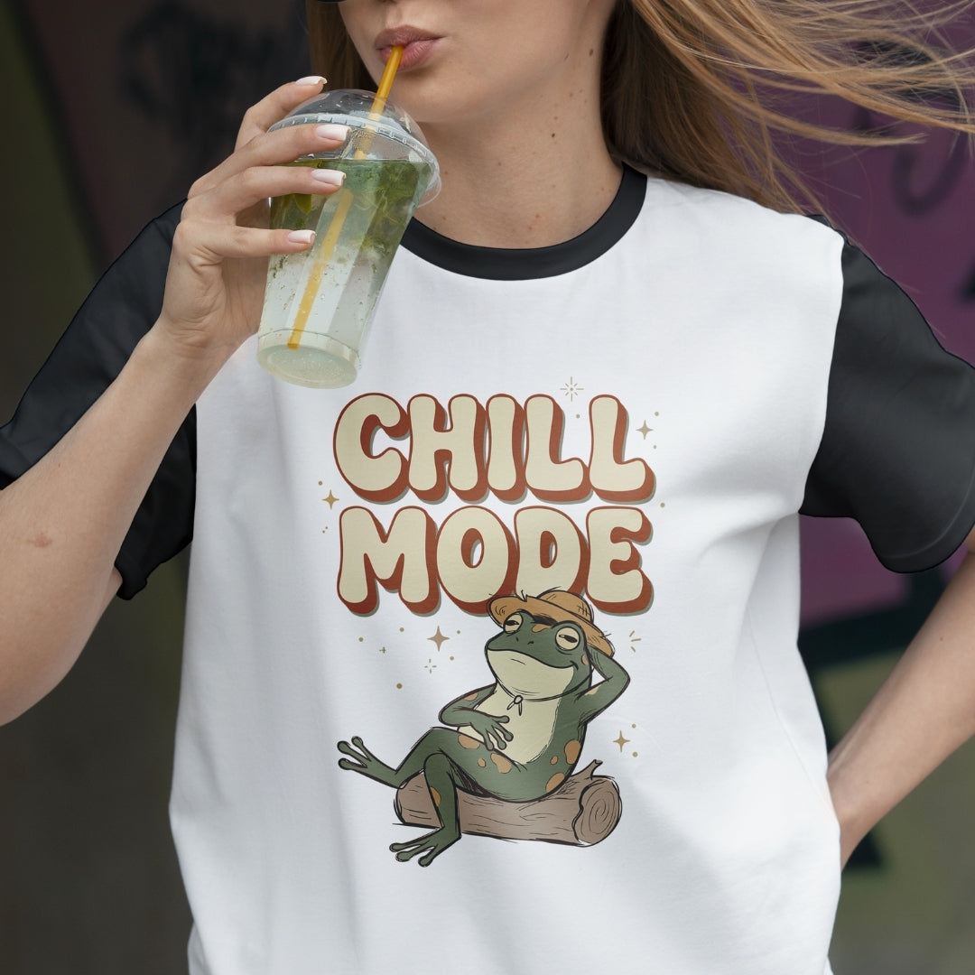 Person wearing a white t-shirt with 'Chill Mode' and a frog graphic, holding a drink.