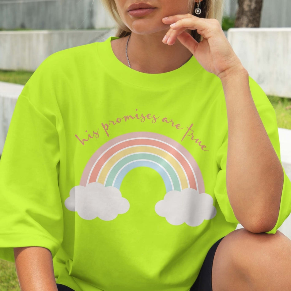 Person wearing a bright green t-shirt with a rainbow and cloud design, sitting outdoors.