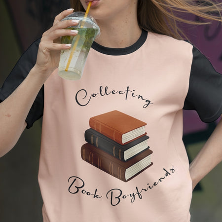 Person wearing a shirt with a book-themed design and text, holding a drink.