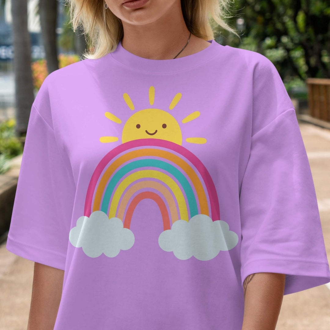 Person wearing a purple t-shirt with a rainbow and sun design outdoors.