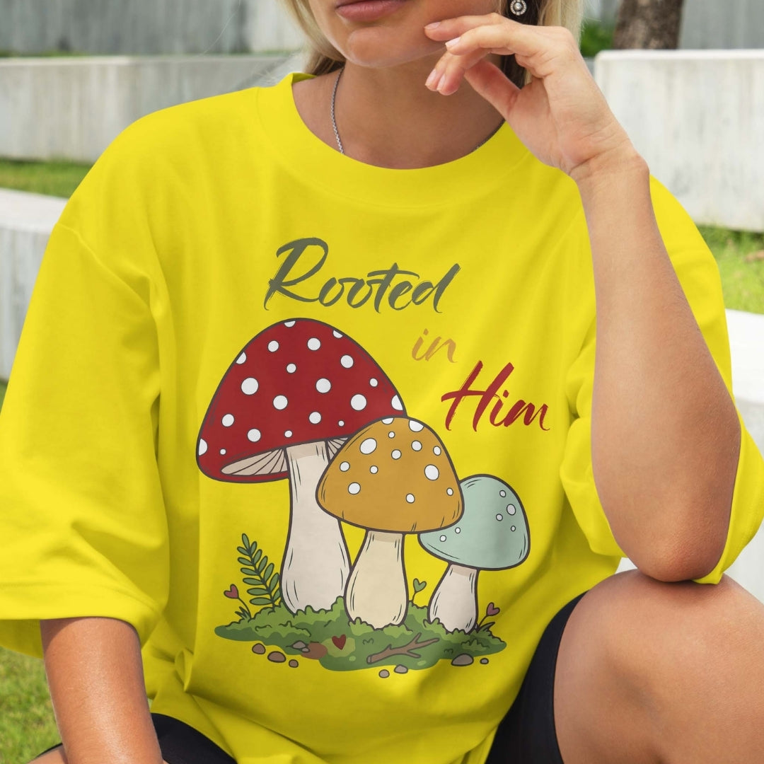 Person wearing a yellow t-shirt with mushroom design and 'Rooted in Him' text outdoors.