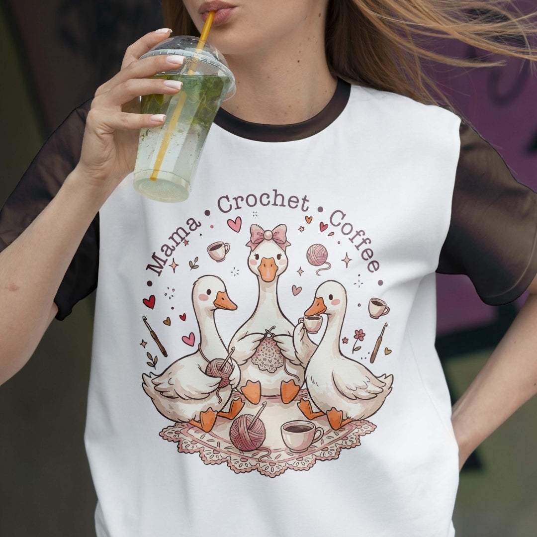 Person wearing a t-shirt with a crochet-themed design and text, holding a drink.