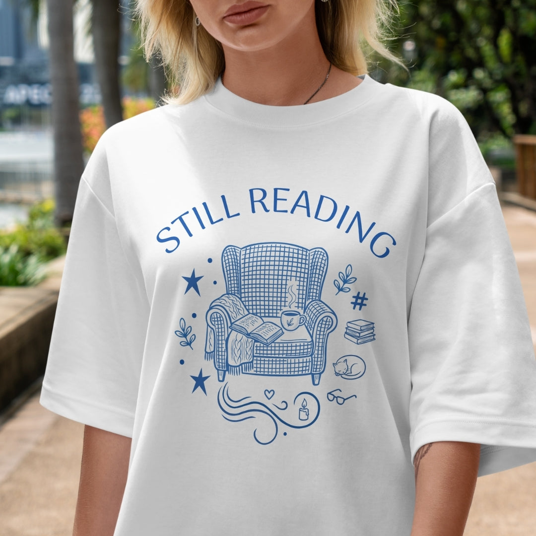 Person wearing a white t-shirt with 'STILL READING' graphic design outdoors.