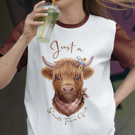 Person wearing a t-shirt with a cow illustration and text, holding a drink.