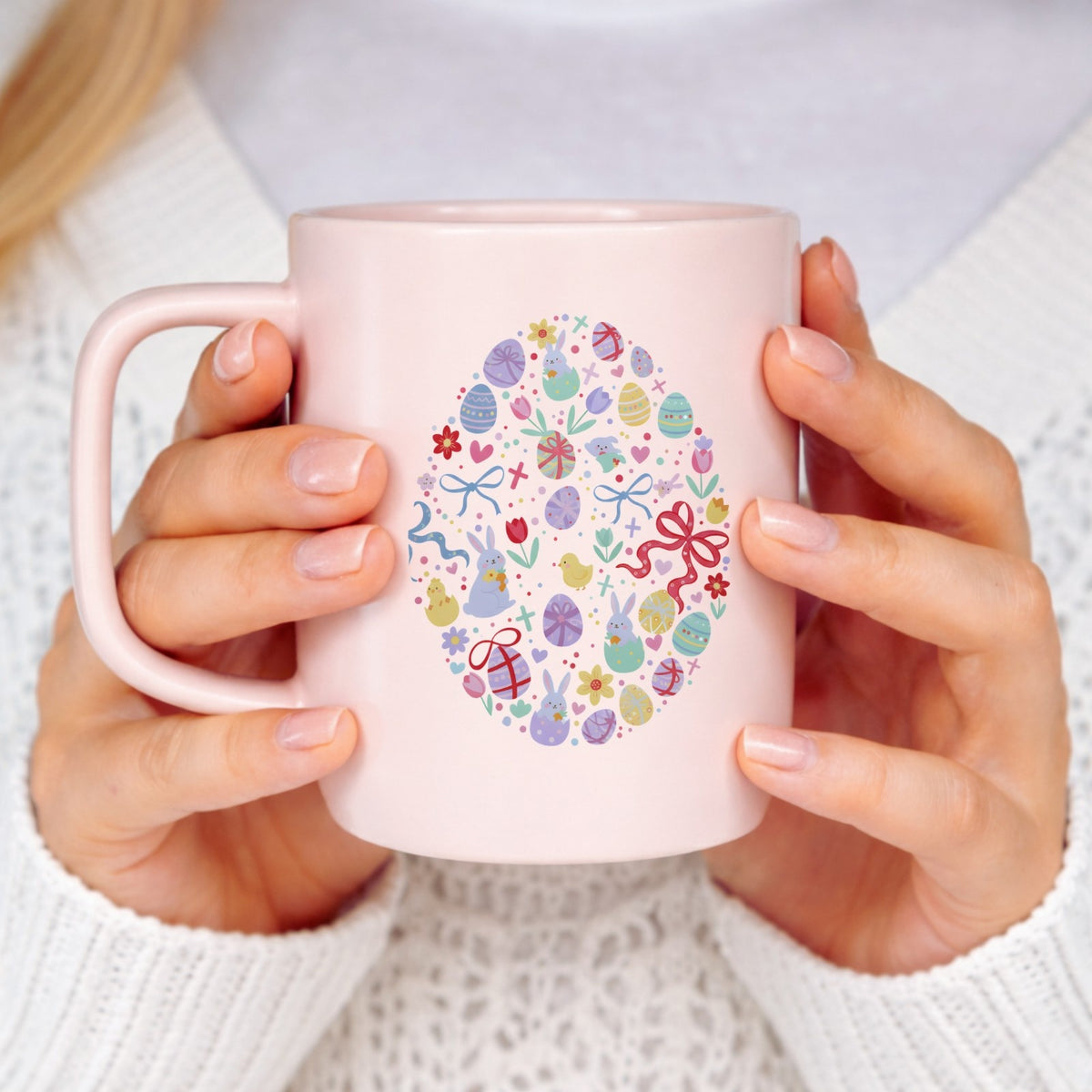 Pink mug with Easter design held by a person wearing a white sweater