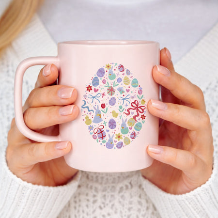 Pink mug with Easter design held by a person wearing a white sweater