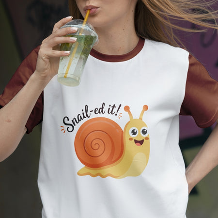 Person wearing a t-shirt with a snail graphic and text, holding a drink.