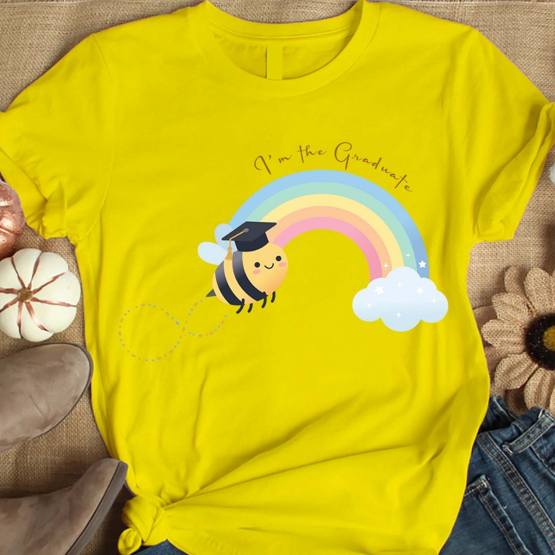Yellow t-shirt with a bee and rainbow graphic, worn by a person sitting on a textured surface.