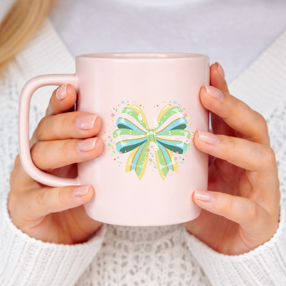 Pink mug with a colorful butterfly design held by a person wearing a white sweater.