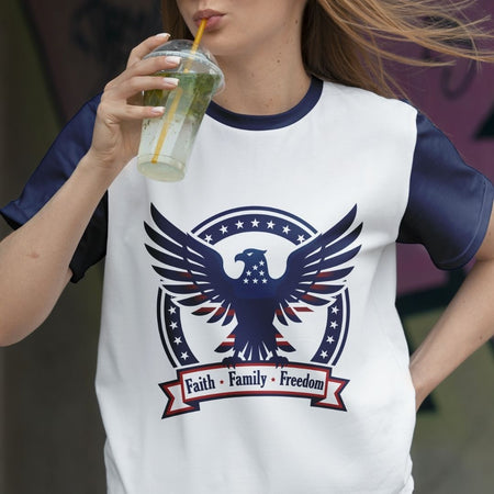 Person wearing a t-shirt with an eagle design and 'Faith Family Freedom' text, drinking from a cup.