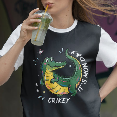 Person wearing a black t-shirt with a colorful alligator graphic and text, holding a drink.