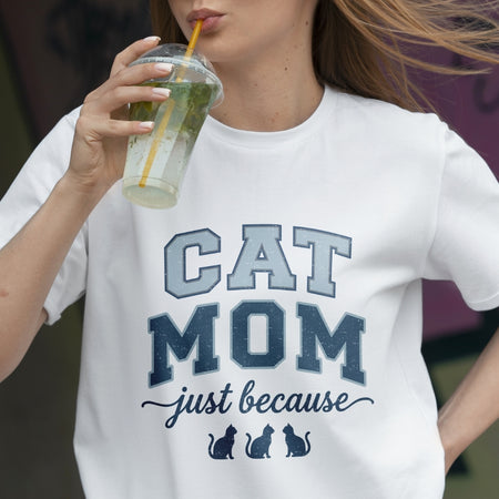 Person wearing a white t-shirt with 'CAT MOM just because' text, holding a drink.