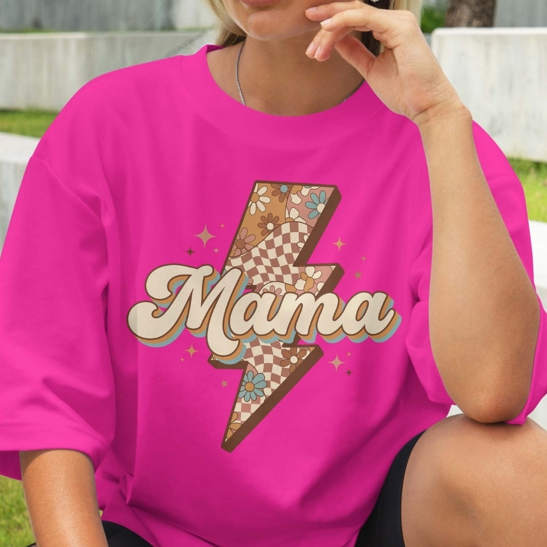 Person wearing a pink t-shirt with a 'Mama' design outdoors.