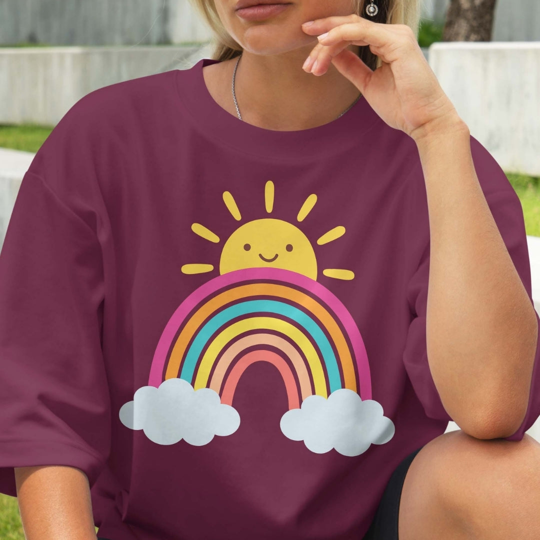 Person wearing a purple t-shirt with a rainbow and sun design outdoors.