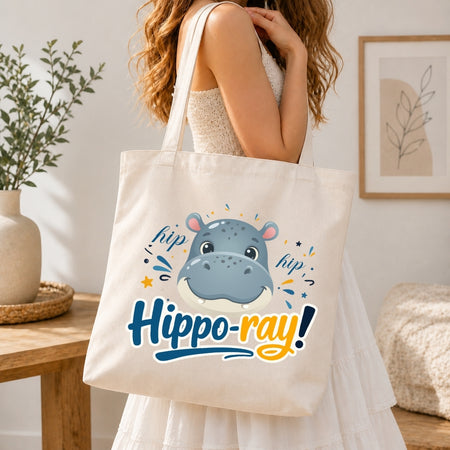 Person holding a tote bag with a hippo design and 'hipp-o-ray!' text in a home setting.