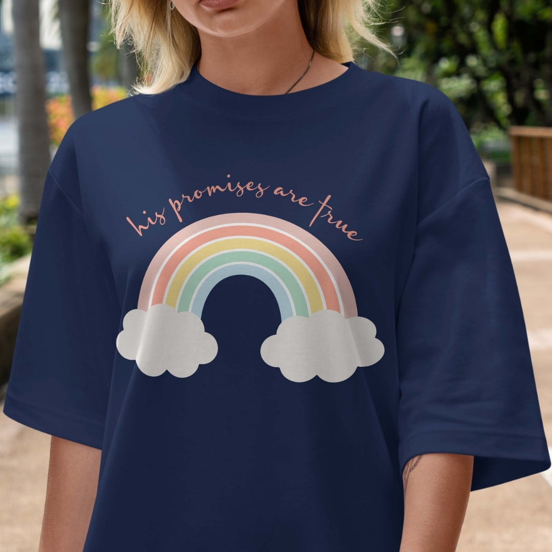 Person wearing a navy blue t-shirt with a rainbow and cloud design and text outdoors.